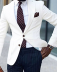 Man wearing a white blazer, patterned tie, and dark pinstripe pants.