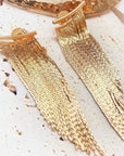 Gold tassel earrings on a textured surface
