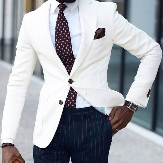 Man wearing a white blazer, patterned tie, and dark pinstripe pants.