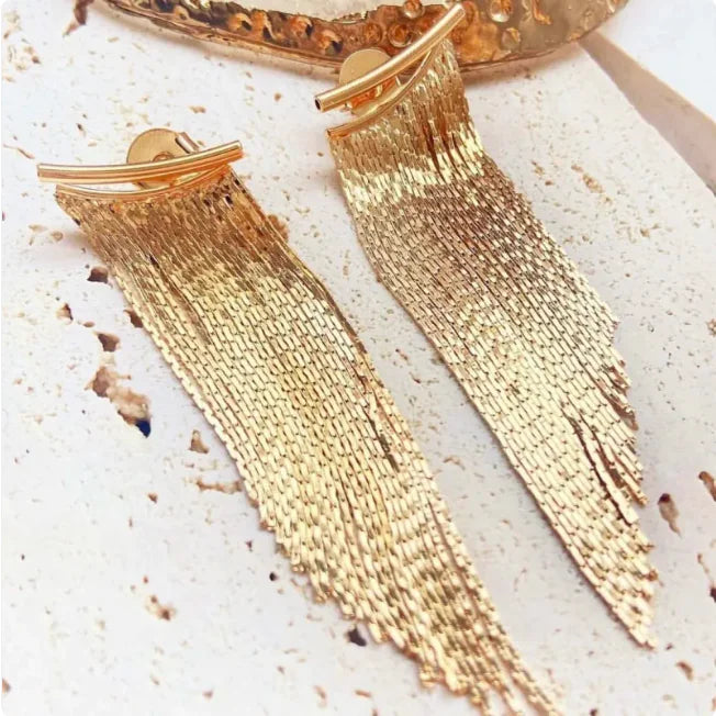 Gold tassel earrings on a textured surface